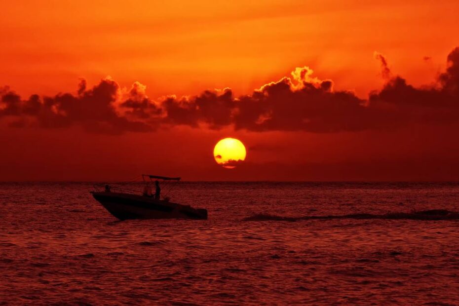 Barco solitario al atardecer en una playa costarricense teñida de rojo y amarillo.