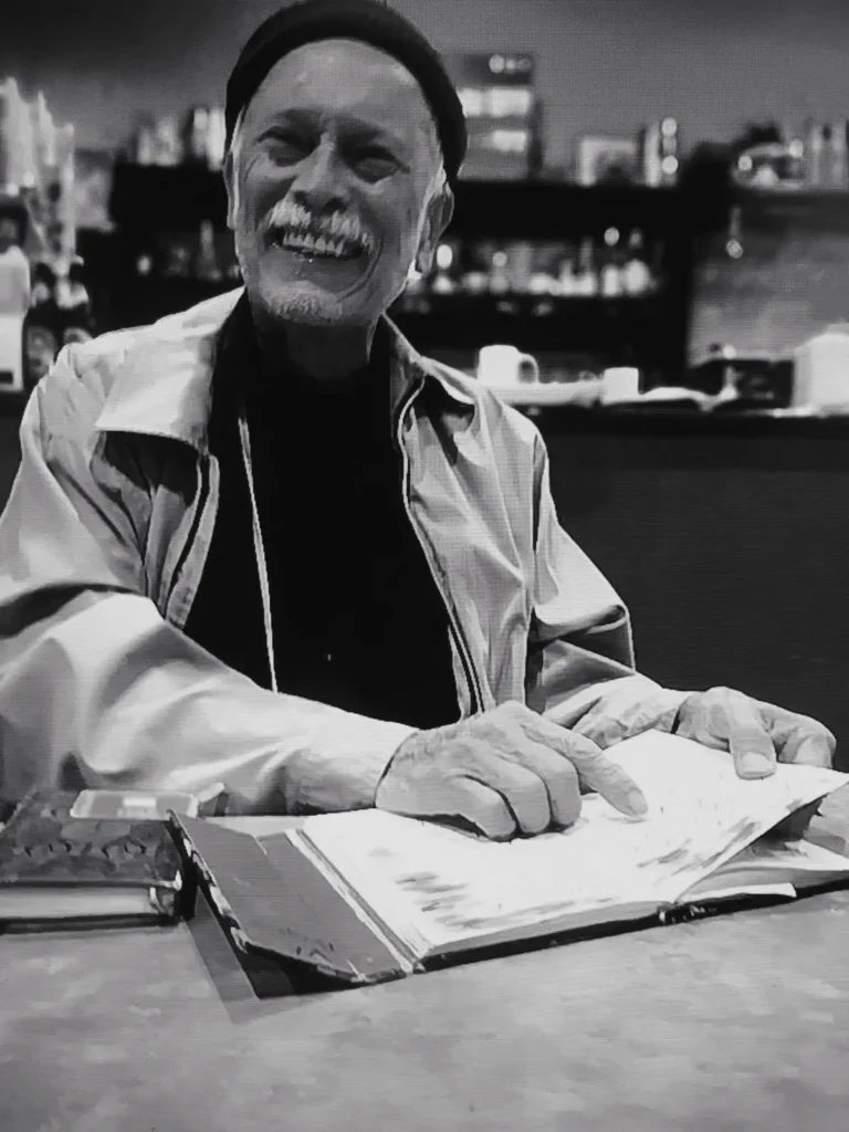 Luis Jorge Poveda sonriente mientras hojea un cuaderno abierto.