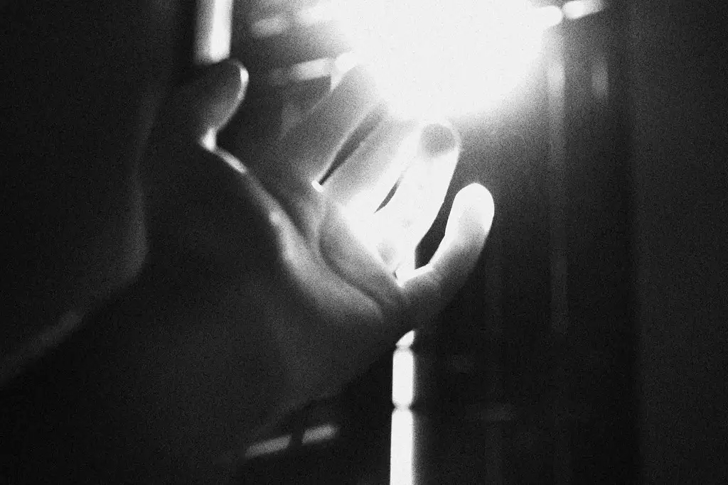 Mano levantada en blanco y negro, alcanzando un haz de luz brillante.