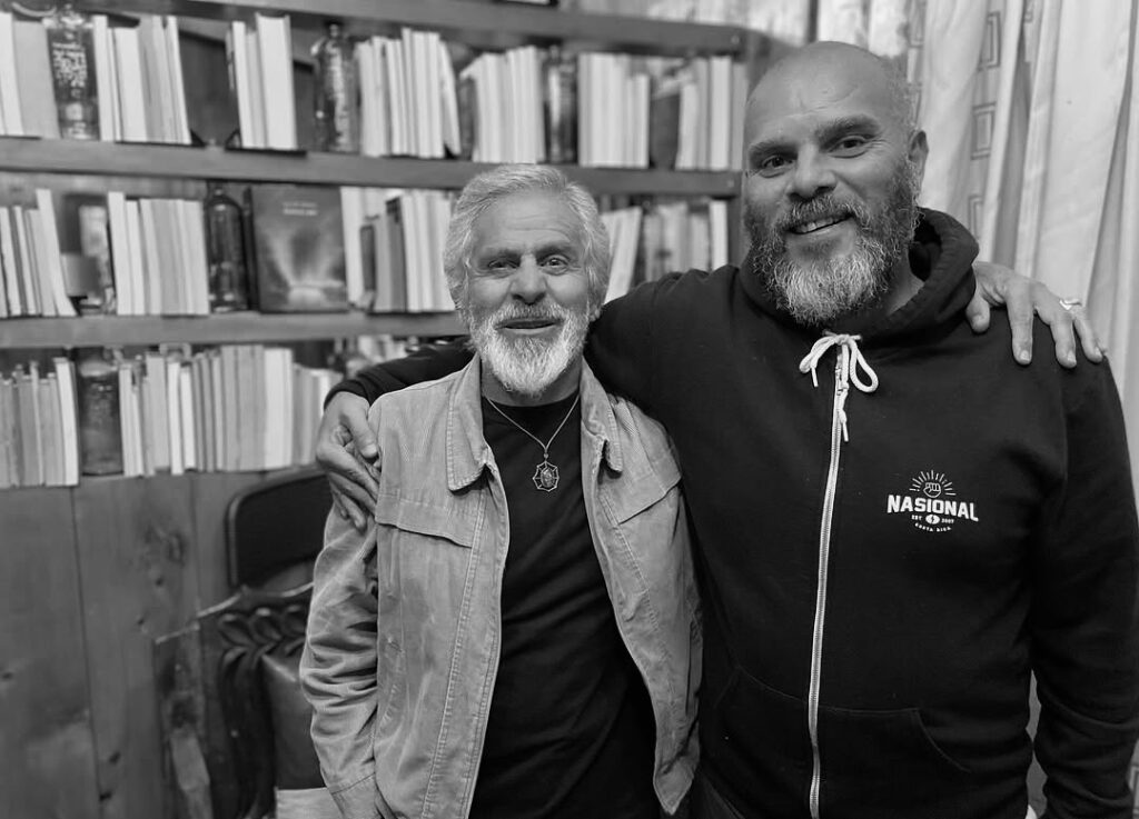Martín Campos y Valdo Jiménez, abrazados, frente a estantes con libros (blanco y negro).