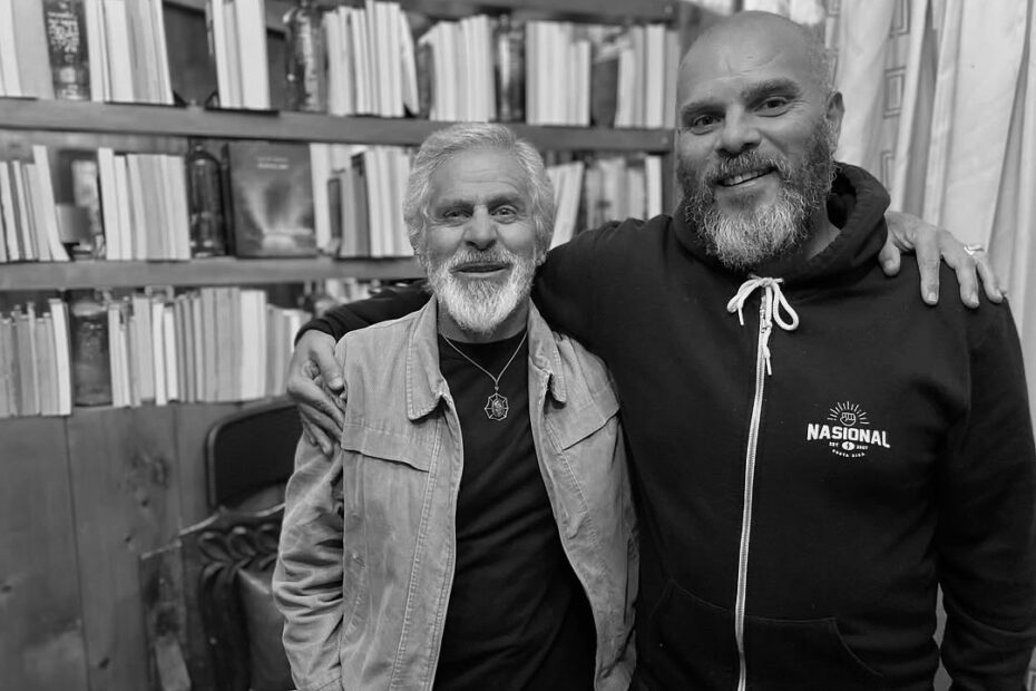 Martín Campos y Valdo Jiménez, abrazados, frente a estantes con libros (blanco y negro).