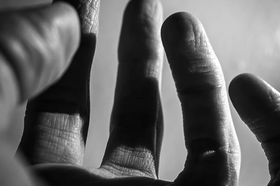 Mano extendida en blanco y negro, iluminada lateralmente, con detalles marcados en la piel.