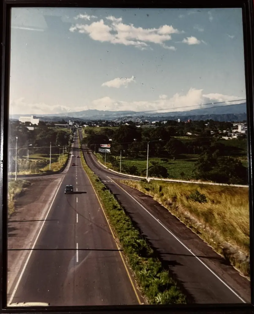 Carretera radial hacia Alajuela en los años 80, vista panorámica con autos y paisajes al fondo.