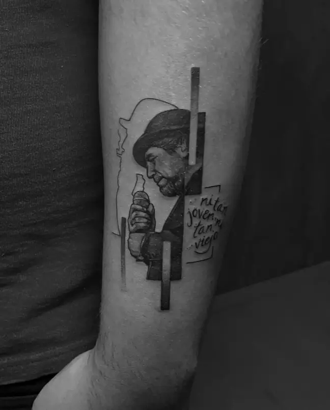 Tatuaje en el antebrazo de Joaquín Sabina con sombrero y micrófono, acompañado de la frase “ni tan joven ni tan viejo”
