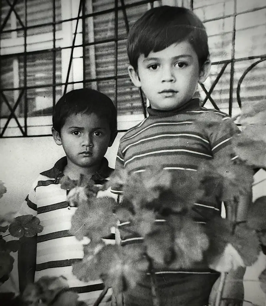 Dos niños posan frente a una ventana enrejada, fotografía en blanco y negro.