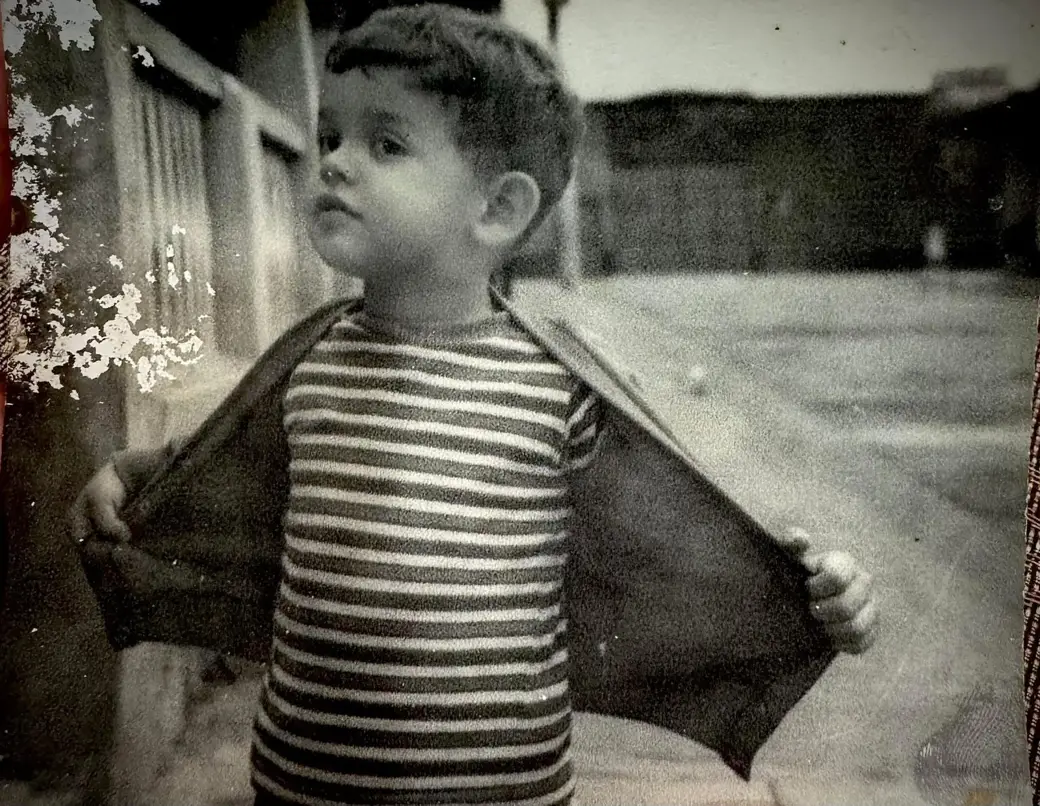 Niño con camiseta de rayas abre su chaqueta en gesto espontáneo, fotografía en blanco y negro.