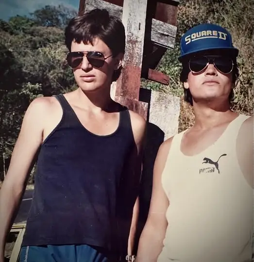 Dos jóvenes con gafas oscuras posando al aire libre, estilo ochentero.