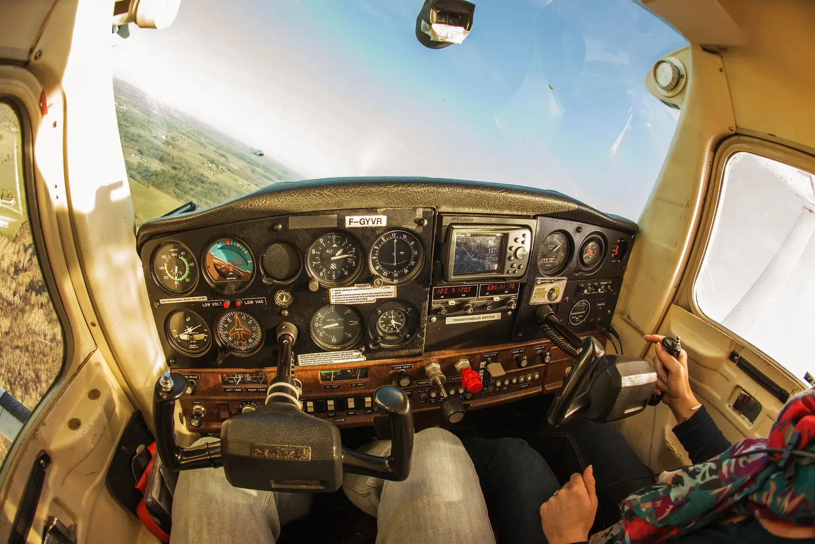 Cabina de avión vista desde el piloto con instrumentos y paisaje al fondo.