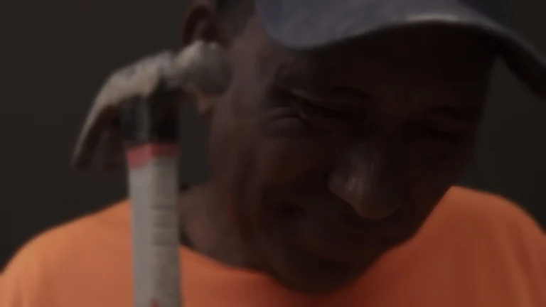 Hombre con gorra sosteniendo un martillo y expresión de dolor.