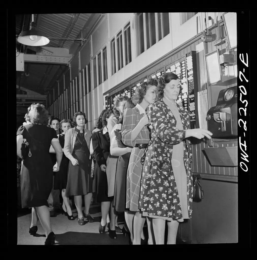 Mujeres en fila marcando tarjeta en una fábrica durante la Segunda Guerra Mundial.