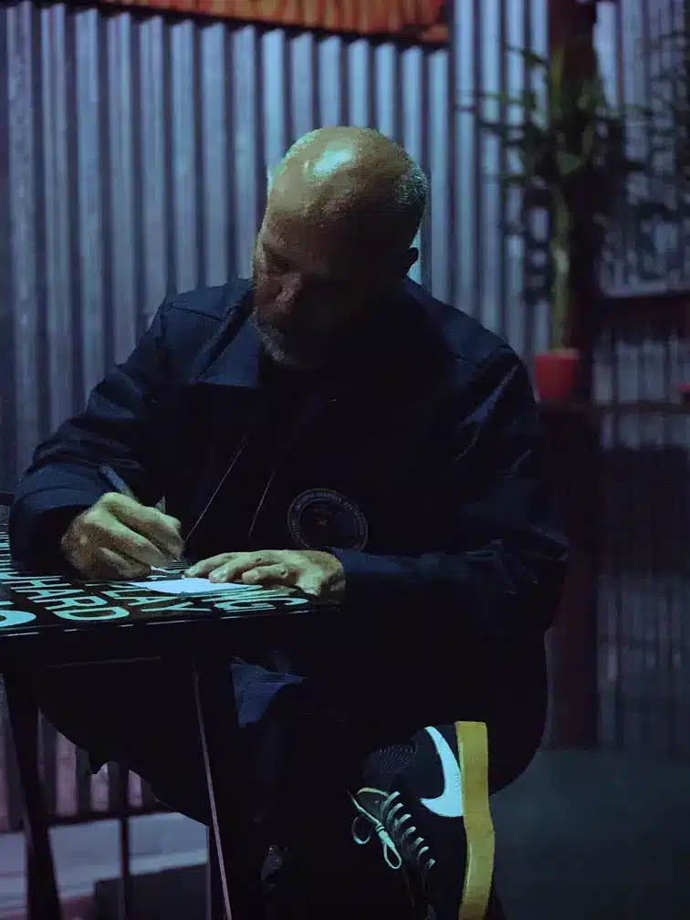 Valdo Jiménez escribiendo en una mesa metálica bajo luz tenue
