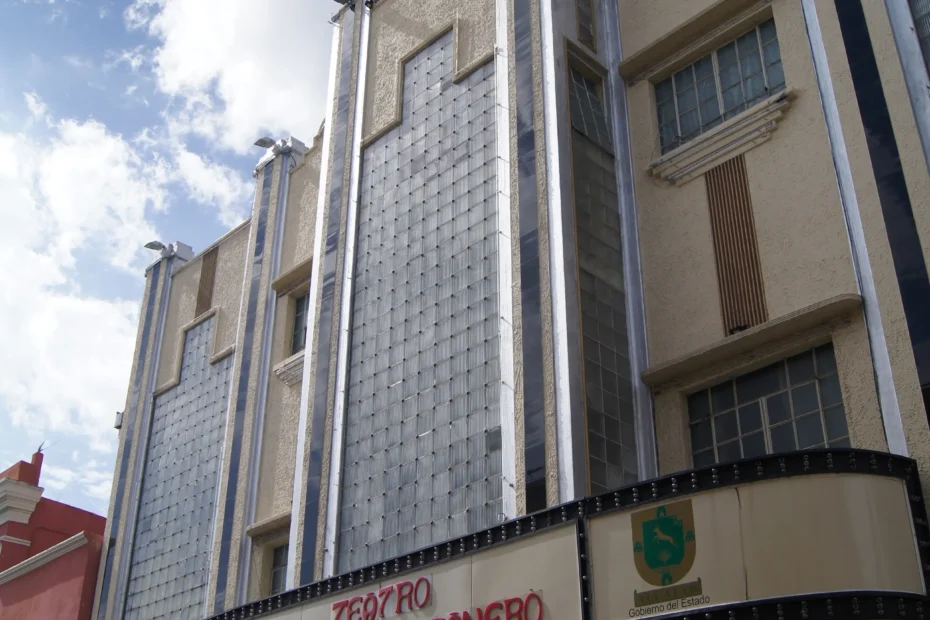 Una foto a color de la fachada de un teatro con un cartel que dice "Teatro Armando Manzanero", bajo un cielo azul con nubes, mostrando un edificio de estilo art déco.