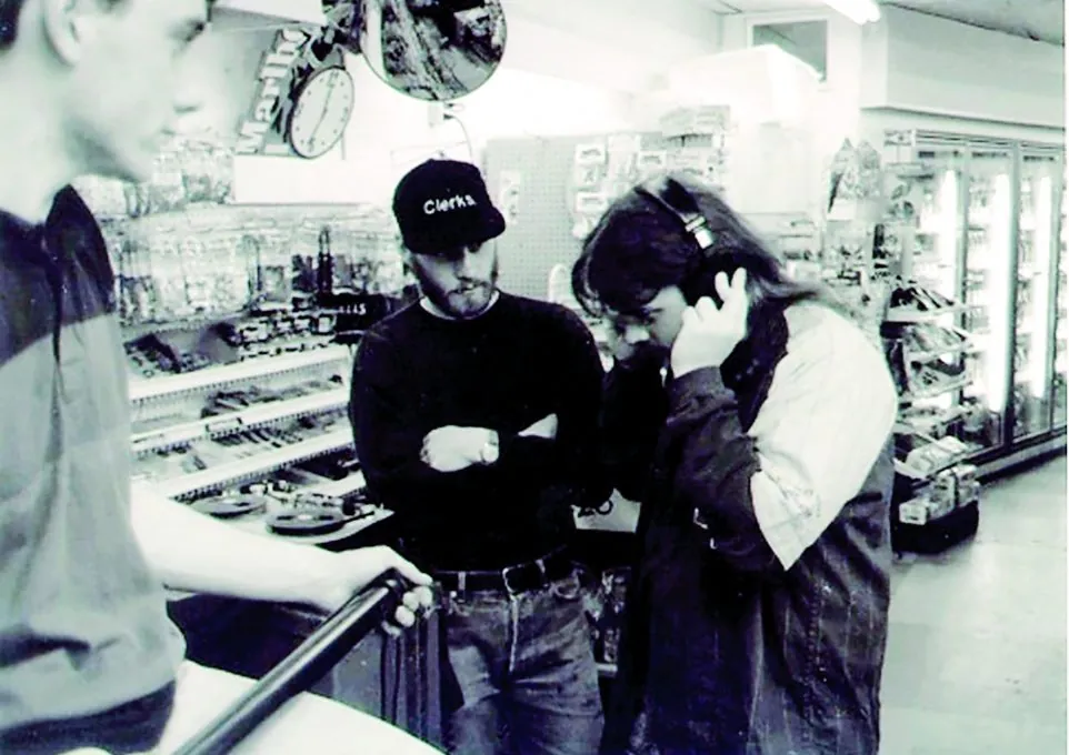 Kevin Smith con gorra de Clerks dirige dentro del mini súper, junto a un sonidista con audífonos.