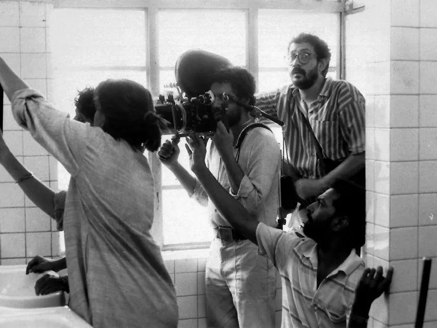 Camarógrafo con la cámara al hombro filmando junto a una ventana en un cuarto de azulejos.