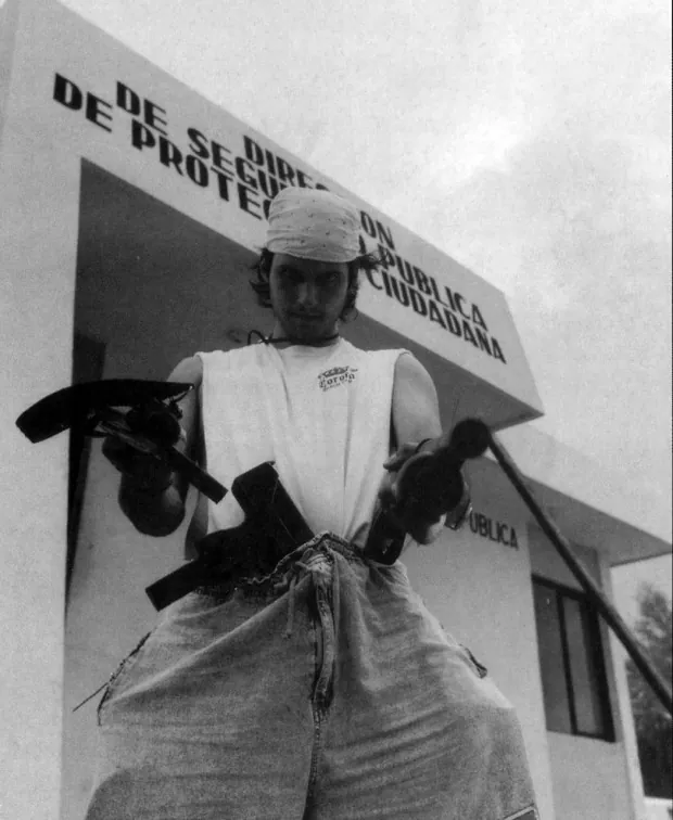 Robert Rodriguez carga armas de utilería frente a un edificio de seguridad pública durante un rodaje en México.